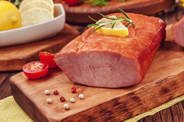 Piece of smoked pork loin with rosemary branch and lemonon the wood cutting board