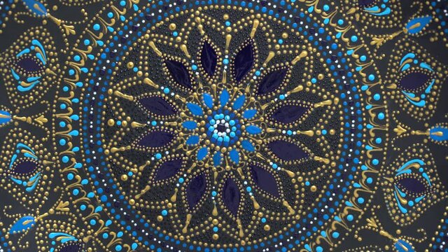 Decorative ceramic plate with black, blue and golden colors, painted plate on background, closeup, top view, rotate. Decorative porcelain plate painted with acrylic paints, handwork, dot painting