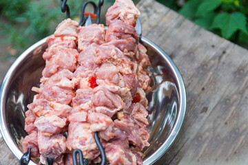 Fresh raw shish kebab in a nickel-plated bowl. Juicy pork meat is strung on skewers and placed on a rough wooden tray in the garden