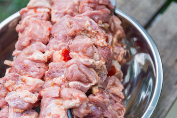 Close up photo of the raw souvlaki with spices in a nickel-plated bowl. Juicy meat of the pork neck is strung on skewers and placed on a rough wooden tray in the garden