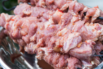 Close up photo of the raw shish kebab with spices in a nickel bowl. Juicy meat of the pork neck is strung on skewers and placed on a rough wooden tray in the garden