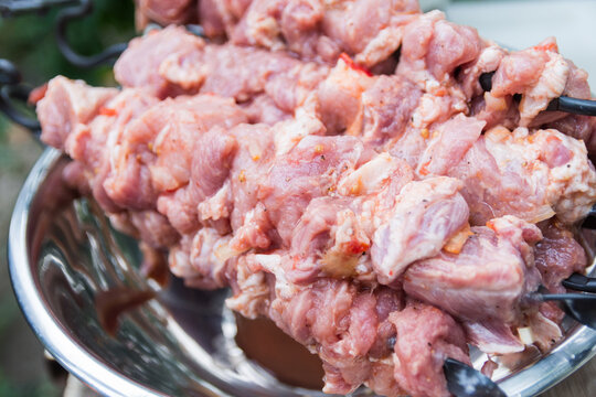 Close Up Photo Of The Raw Shish Kebab With Spices In A Nickel Bowl. Juicy Meat Of The Pork Neck Is Strung On Skewers And Placed On A Rough Wooden Tray In The Garden