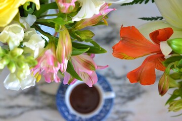 Overhead image of two bouquets of flowers in the foreground and a cup of coffee on a marble table seen in the background of the photo