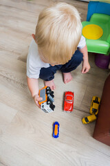 Little young caucasian boy plays with colorful toy cars indoors. Child playing colorful multi-colored machines on the floor. Early development and learning. Bright toys for the toddler game. Education