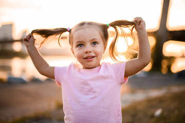 portrait of little blonde girl with two ponytails on her head who holds her hair with her hands
