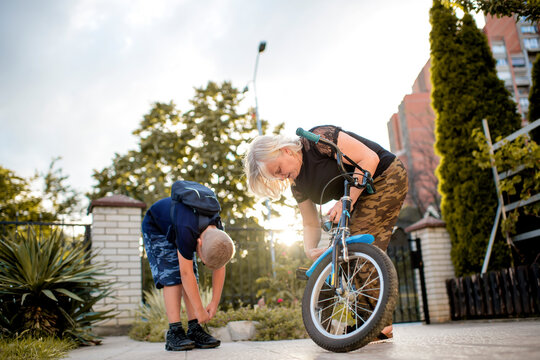 Grandmother helping young boy to fix bike outdoors in garden