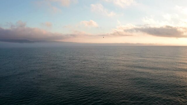 Aerial video over а morning calm sea, beautiful sunrise with low clouds and a lone bird in the sky