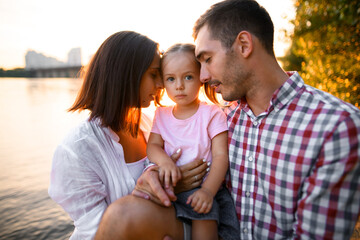 Fototapeta premium Lovely family portrait of mother and father and little cute daughter on summer day.