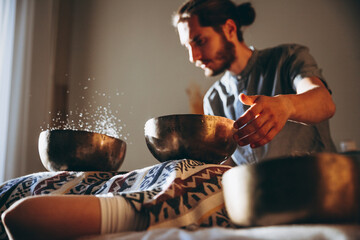 Nepal Buddha copper singing bowl at spa salon. Young bearded man doing massage therapy singing...