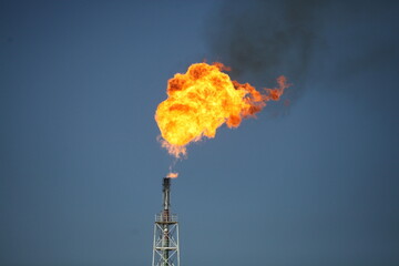 Oil refinery plant. Giant gas torch with black smoke and loud noise. Blue sky background. 