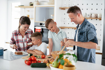  Mother and father making breakfast with sons. Young family preparing delicious food in kitchen.