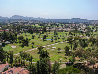 Fototapeta na wymiar Aerial view of golf in middle class neighborhood surrounded with residential house, and mountain on the background in San Diego, South California, USA.