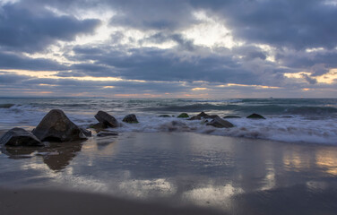 Foaming wave breaking at sunrise with rocky shoreline