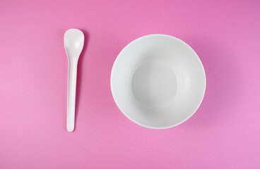 White bowl and white spoon on a pink background.
