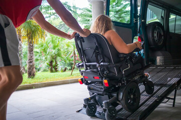 Woman on wheelchair using a vehicle ramp. Accessible transport with assistant driver.