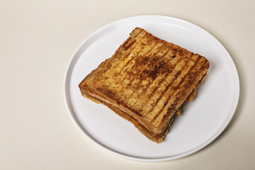 Sandwich with cheese on a round white plate on a beige background. Copy space.