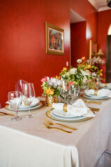 Elegant table setting with gold accents and red wall, clear chairs and flowers