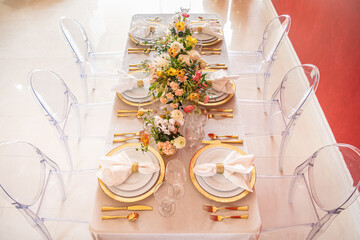 Elegant table setting with gold accents and red wall, clear chairs and flowers