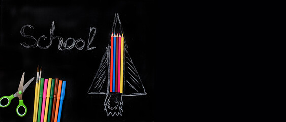 Back to school concept, drawing rocket from colored pencils on a blackboard with word school on it.