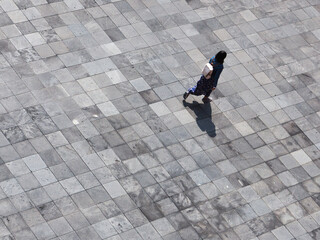 Mujer caminando. Vista aérea de estudiante en entorno amplio de acabado gris. Captura horizontal. 