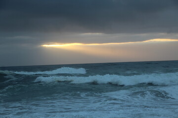 Obraz premium Ocean waves with sun peaking through clouds