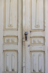 Old white peeling door. There is a lock and a handle in the form of a ball on the door.