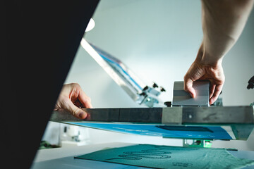 Selective focus of artisan working on screen printing machine and textile in workshop 