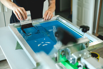 Selective focus of man applying plastisol ink on stencils on screen printing press in workshop 