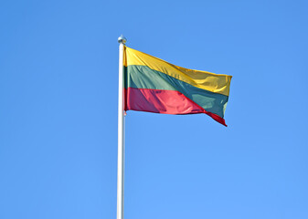 The national flag of Lithuania flies against the background of the blue sky