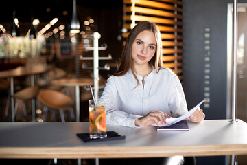 girl sits at a table in a cafe and holds documents in her hands