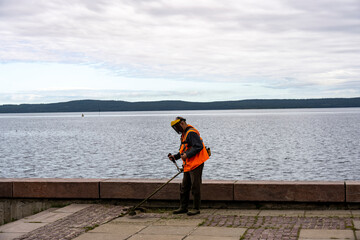a worker in an orange jacket cleans on the embankment