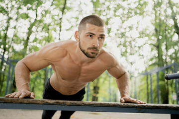 a satisfied man of athletic build does the plank exercise on the simulator thinks about his body and health. . stadium in the Park. short hair, beard, naked torso. Caucasian appearance