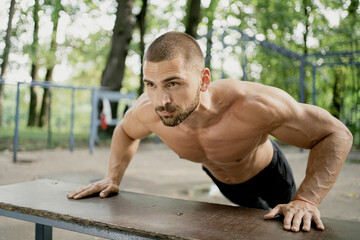 Obraz premium doing the plank exercise on the simulator thinks about your body and health. a satisfied man of athletic build. stadium in the Park. short hair, beard, naked torso. Caucasian appearance