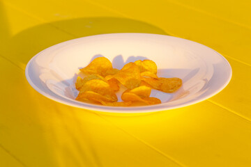 Daylight. yellow wooden background on it a plate of white color. Chips in it.