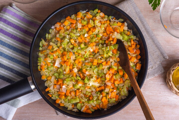 The preparation of fried vegetable filling of onions carrots and celery - ready Mirepoix or Soffritto in a pan, top view.