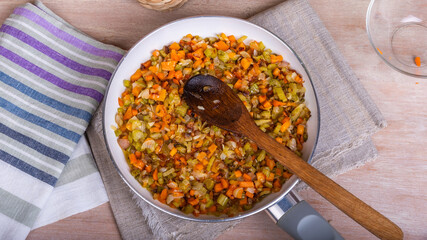 The preparation of fried vegetable filling of onions carrots and celery - ready Mirepoix or Soffritto in a pan, top view.