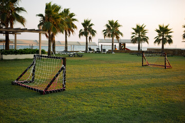 Empty small kids soccer field on vacation at sunset with beautiful green grass. Palm trees in the background. Football. Leisure. Active games. sport. Relax. Weekend. Bright setting sun. Resort