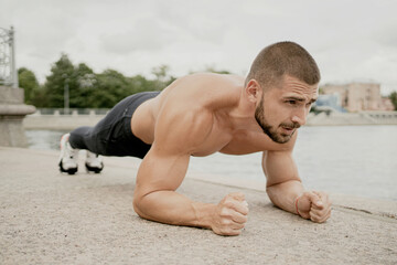Obraz premium portrait of a sporty dark-haired man doing a plank exercise on the street, tense looking ahead. short haircut brunette barbershop. Caucasian appearance