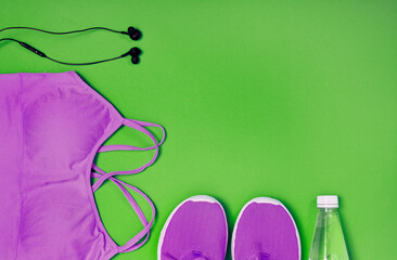Violet sport shoes, crop top, earphones and bottle of water on a green background. Concept of healthy lifestyle, sport and diet. Text space. Top view.