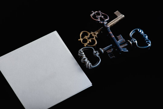 Vintage keys and a piece of white sheet of paper on a black background, low key, there is a place for an inscription