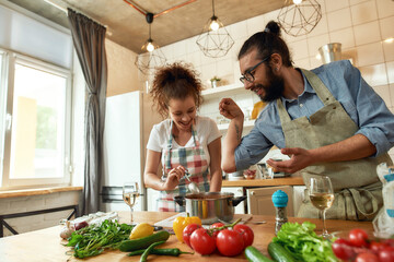 Italian man adding pepper, spice to the soup while woman stirring it and smiling, couple preparing...