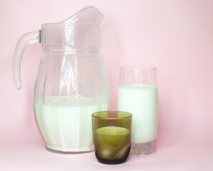 Natural whole milk in a jug and a glass isolated on a pink background closeup