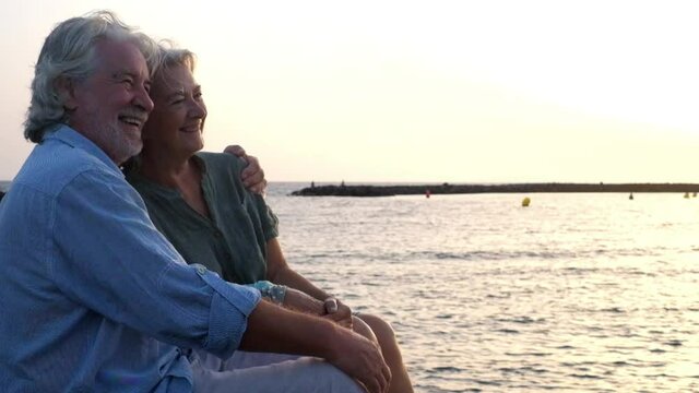 close up and portrait of two happy and active seniors or pensioners having fun and enjoying looking at the sunset smiling with the sea at the background - old people outdoors enjoying vacations
