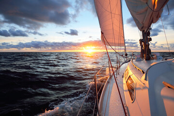Yacht sailing in an open sea at sunset. Close-up view of the deck, mast and sails. Clear sky after...