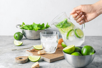 Woman pouring fresh mojito in glass on table