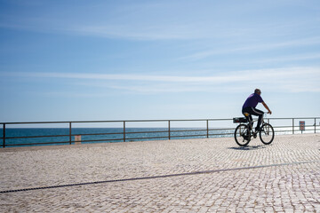 Bicyclist riding along the beach sunshine blue sky outdoors background, person back view.