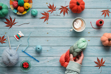 Seasonal Fall flat lay on faded light blue wood boards. Hand holding wool bundle and cup of coffee....