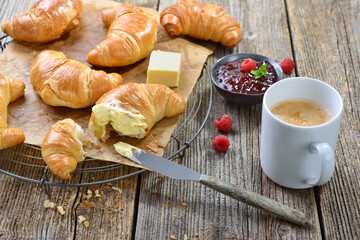 Rustikales Croissant-Frühstück mit Butter, Marmelade und einem Haferl Kaffee Crème - Breakfast with freshly baked croissants on a cooling rack, served with butter,  jam and a cup of coffee creme 