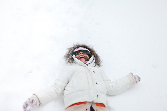 Smiling girl with fur hood laying in snow