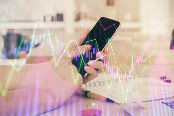 Double exposure of man's hands holding and using a digital device and forex graph drawing. Financial market concept.